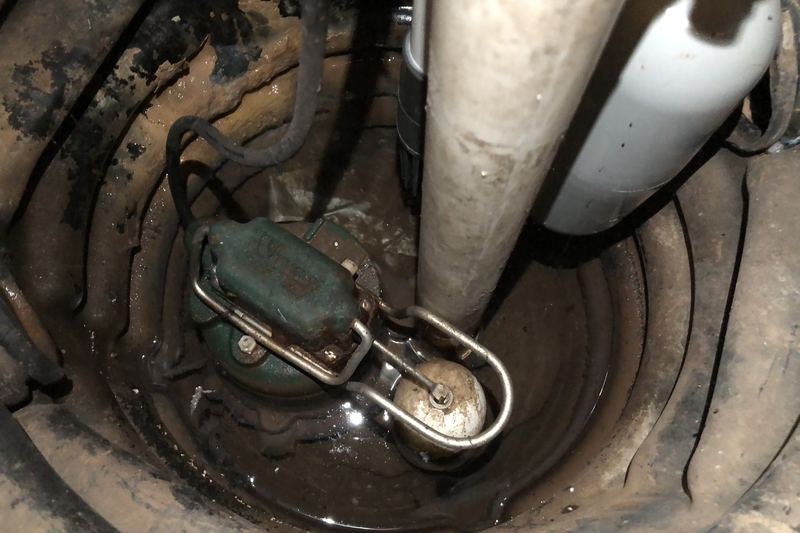 Close-up of a new submersible sump pump and float switch in a basement pit